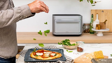 A person adding spices to pizza in front of Brava oven