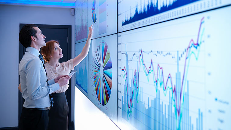 Man and woman viewing charts on wall monitors