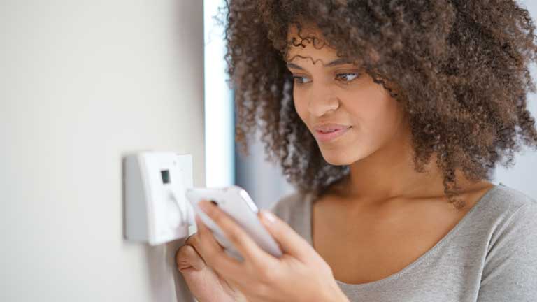 Woman controlling thermostat temperature via mobile device