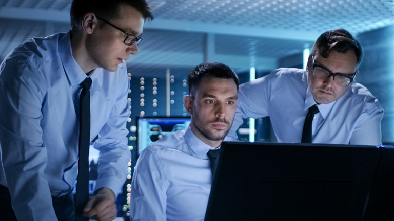 Thee men standing around a computer monitor